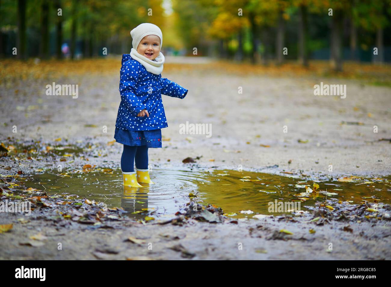 Child wearing yellow rain boots and jumping in puddle on a fall day ...