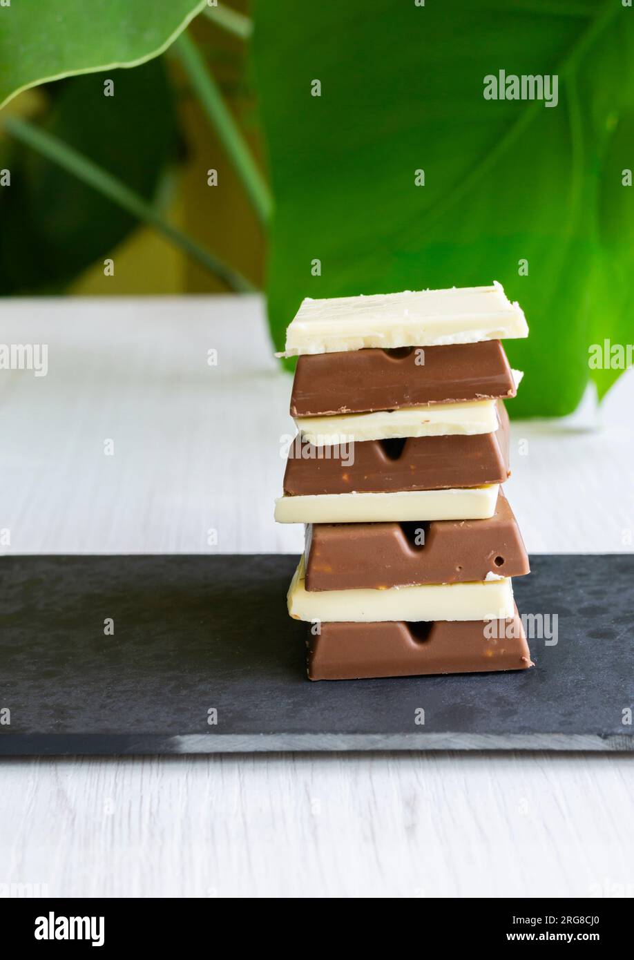 White, milk and dark chocolate squares stacked on a slate tray with a green leaf in the background. Vertical shot. Stock Photo