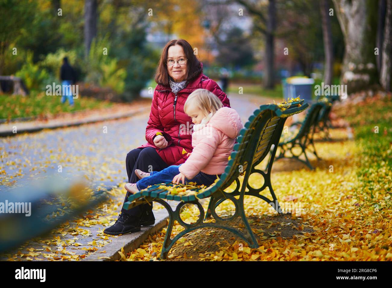 Happy smiling woman with toddler girl on fall day in park. Beautiful family of two in bright red foliage. Grandmother and granddaughter together. Autu Stock Photo