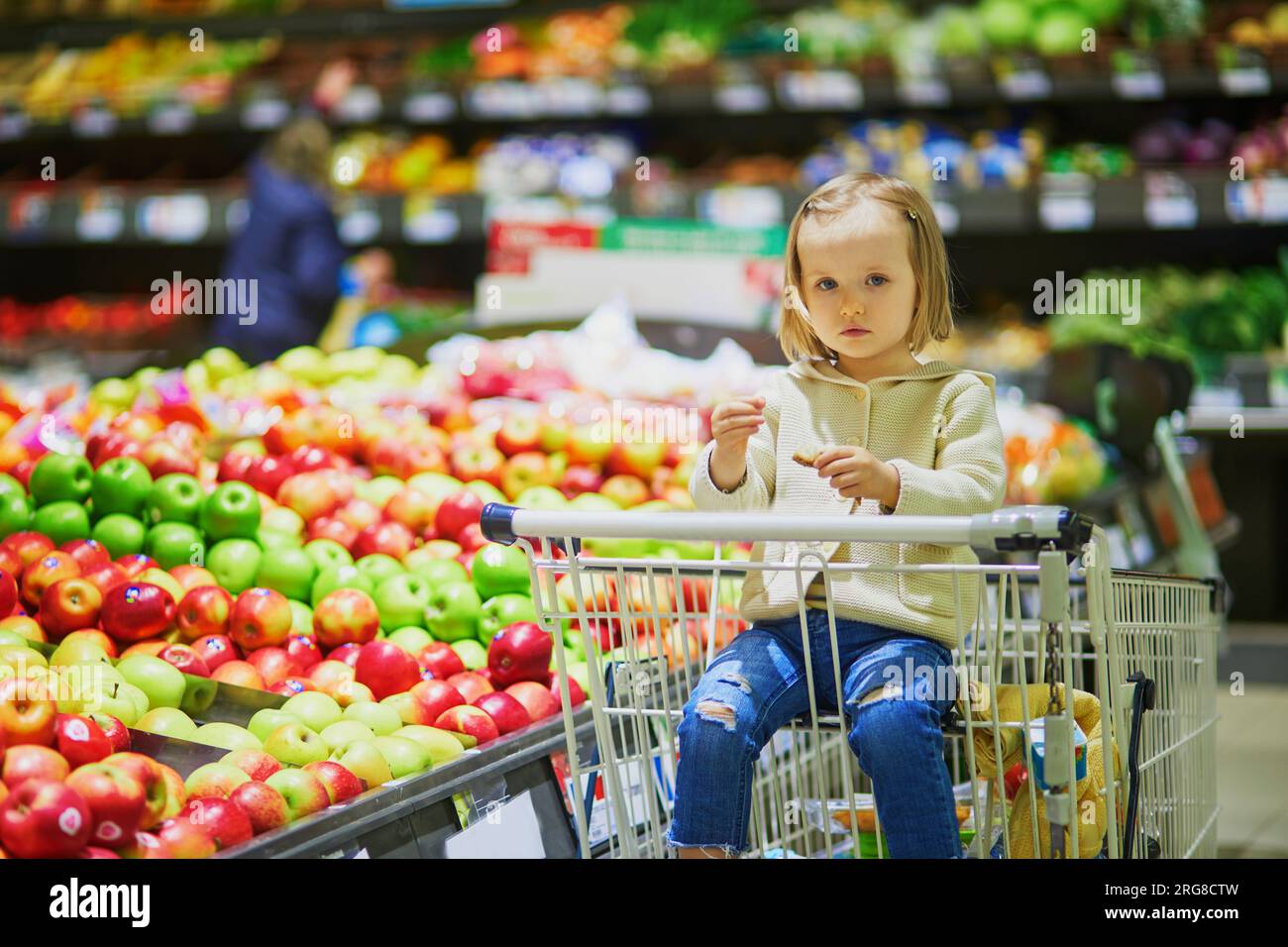 Adorable toddler girl sitting in the shopping cart in a food store or a ...