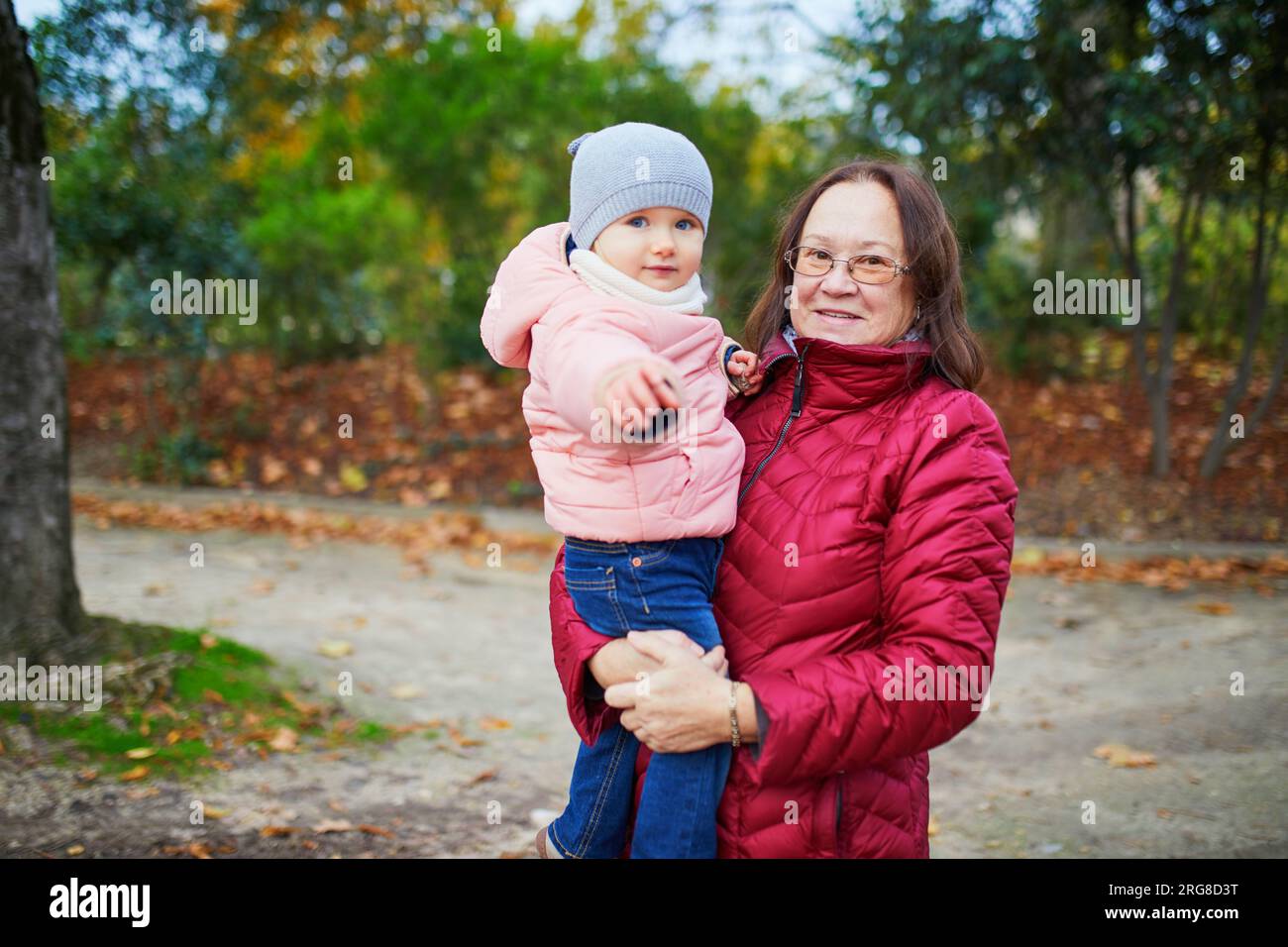 Happy smiling woman with toddler girl on fall day in park. Beautiful family of two in bright red foliage. Grandmother and granddaughter together. Autu Stock Photo