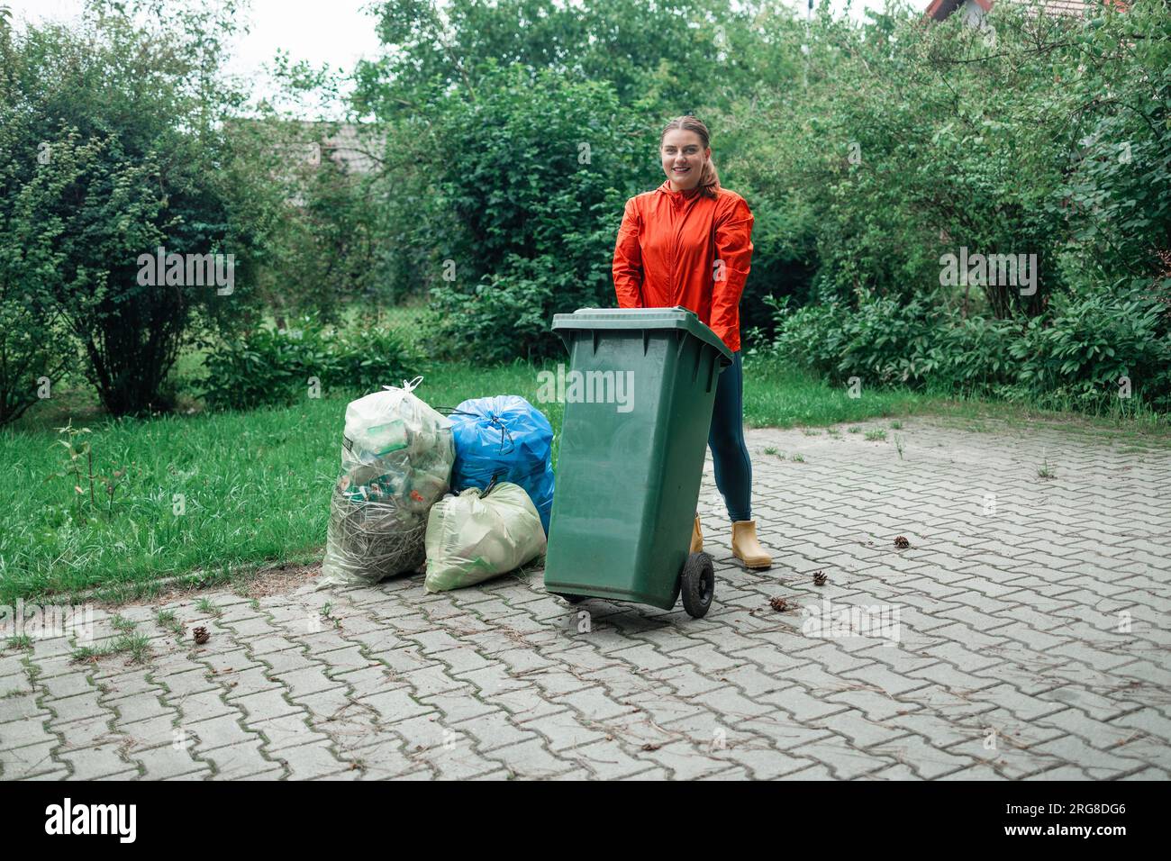 Adult woman household taking out bin to the street on rubbish day. Stock Photo