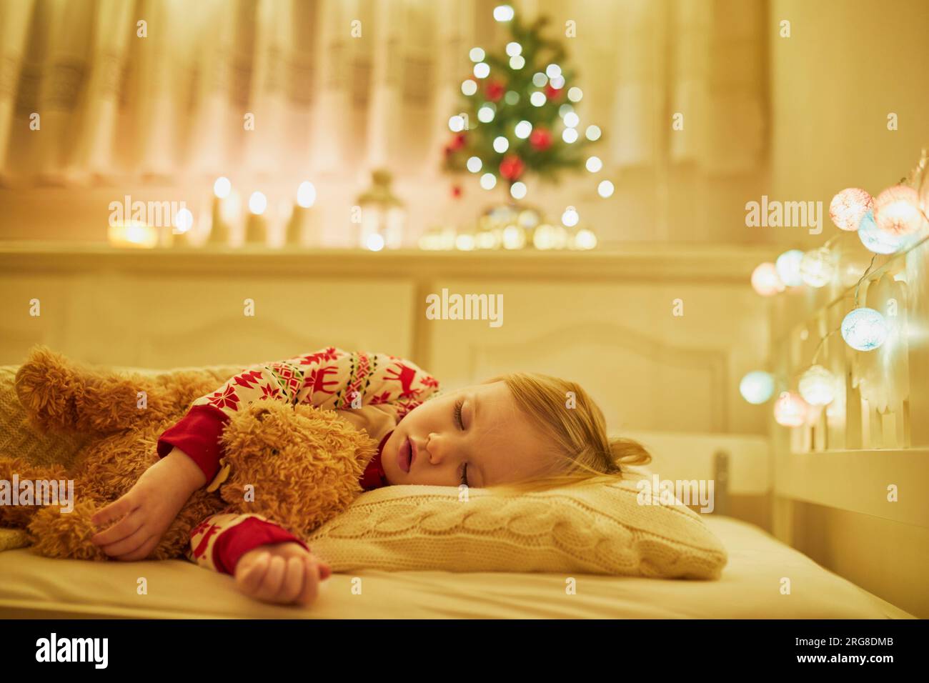 Adorable toddler girl sleeping with her teddy bear under the Christmas