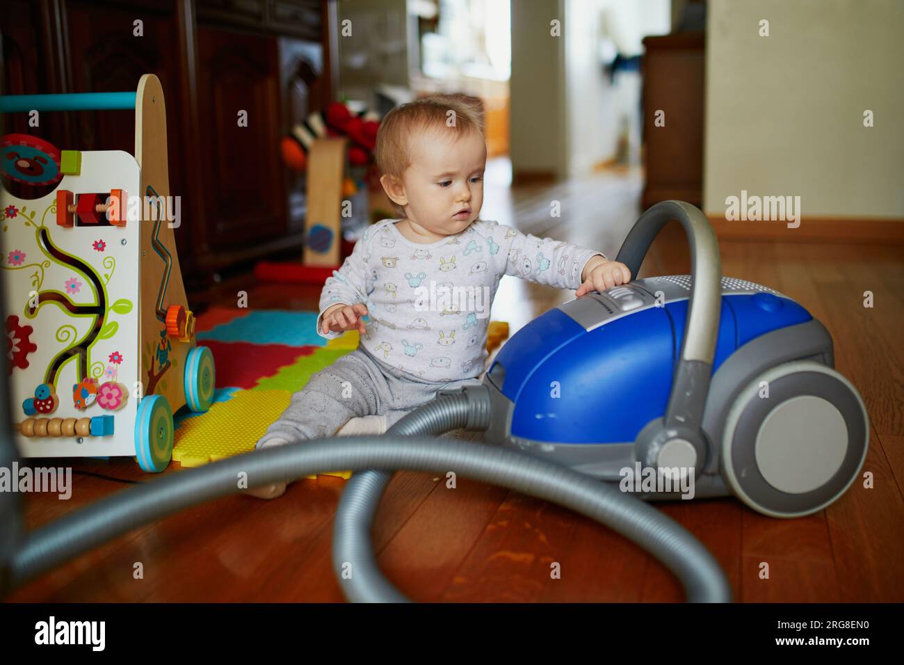 Little baby girl playing with vacuum cleaner at home. Toddler helping