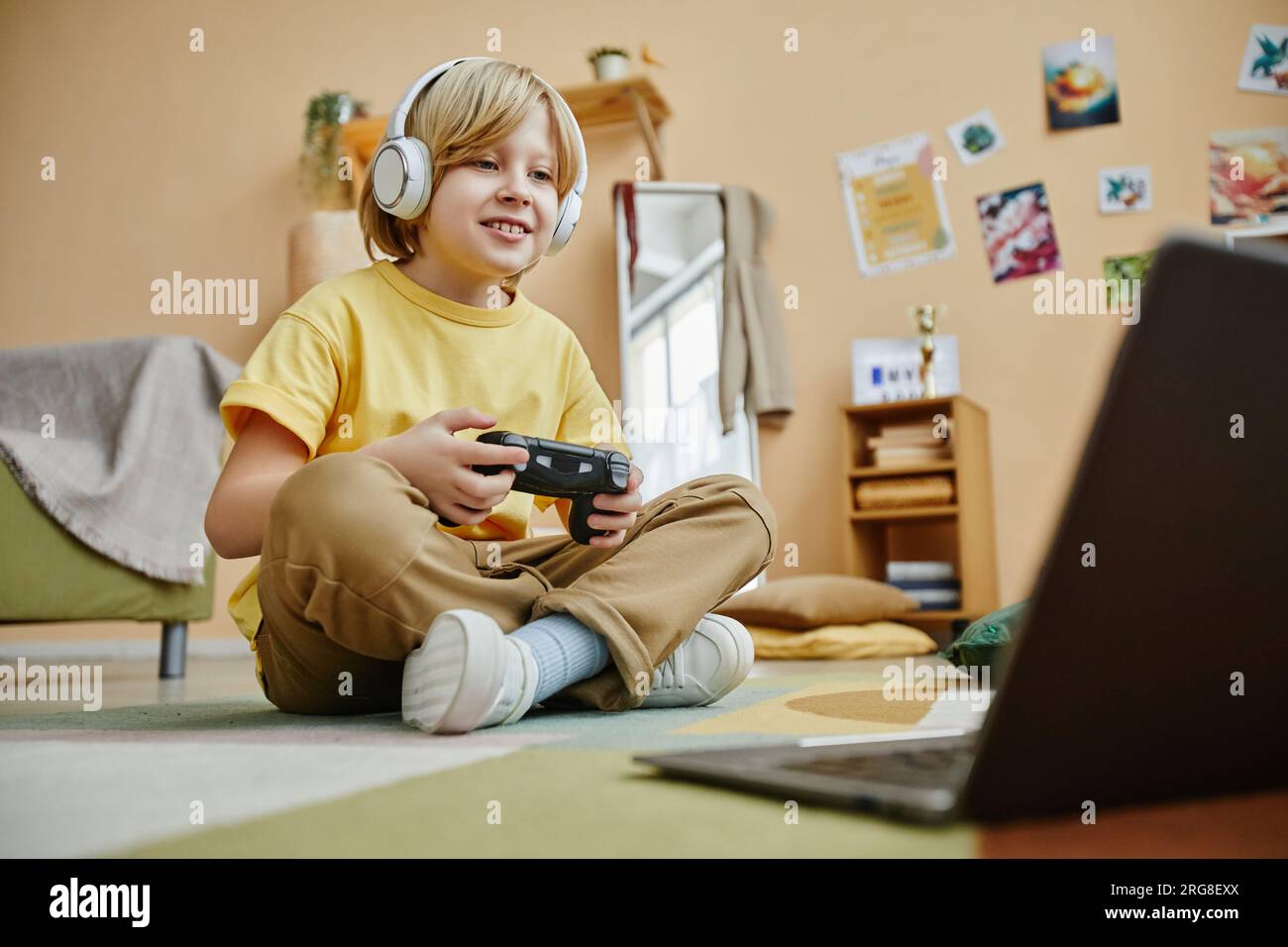 Cute smiling boy in headphones pressing gamepad buttons while sitting ...