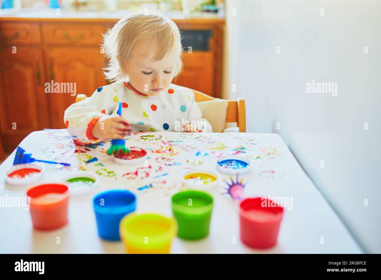 Adorable little girl painting with fingers at home, in kindergaten or preschool. Creative games for kids staying at home Stock Photo