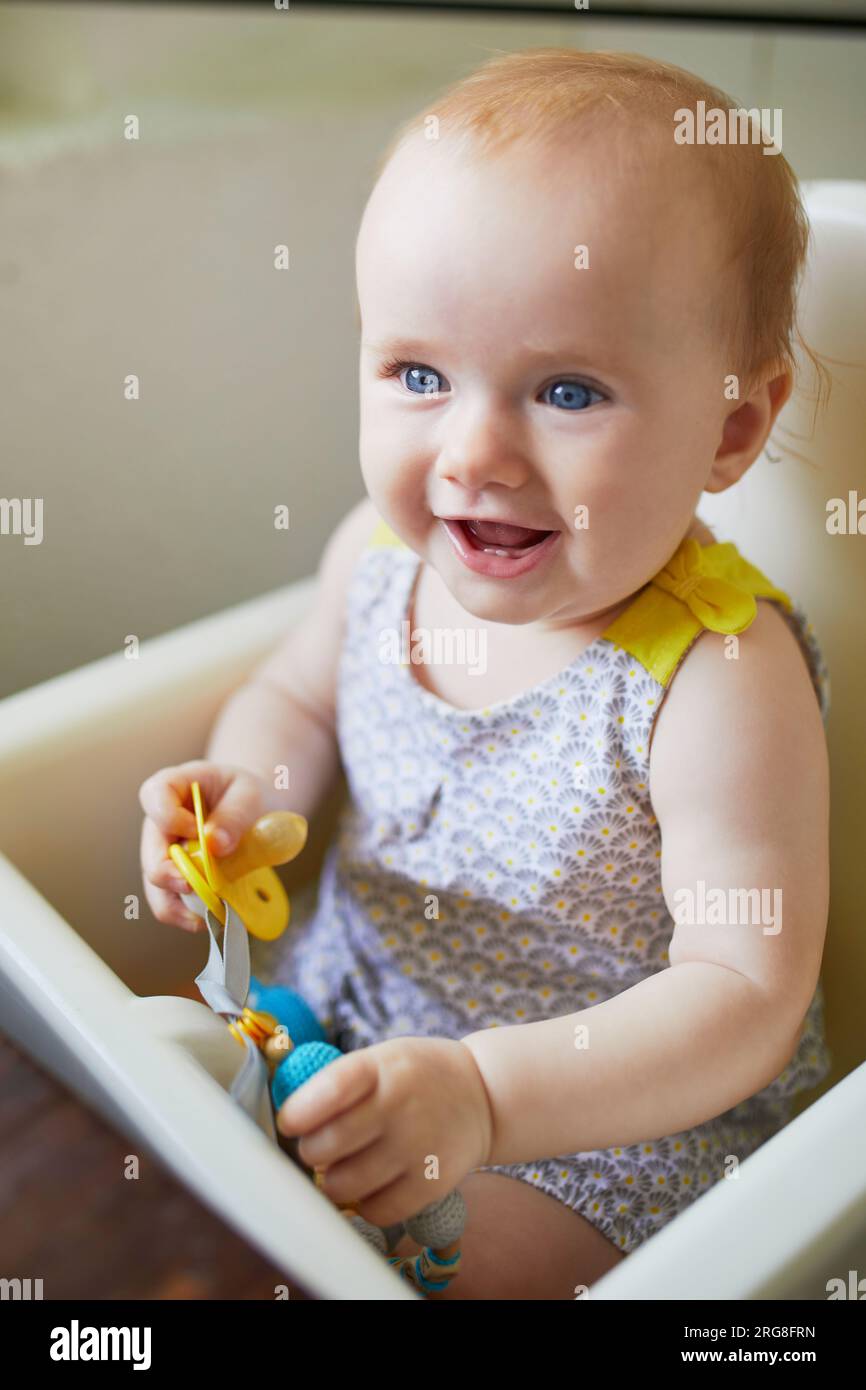 Little baby girl sitting in high chair in cafe, restaurant or at home