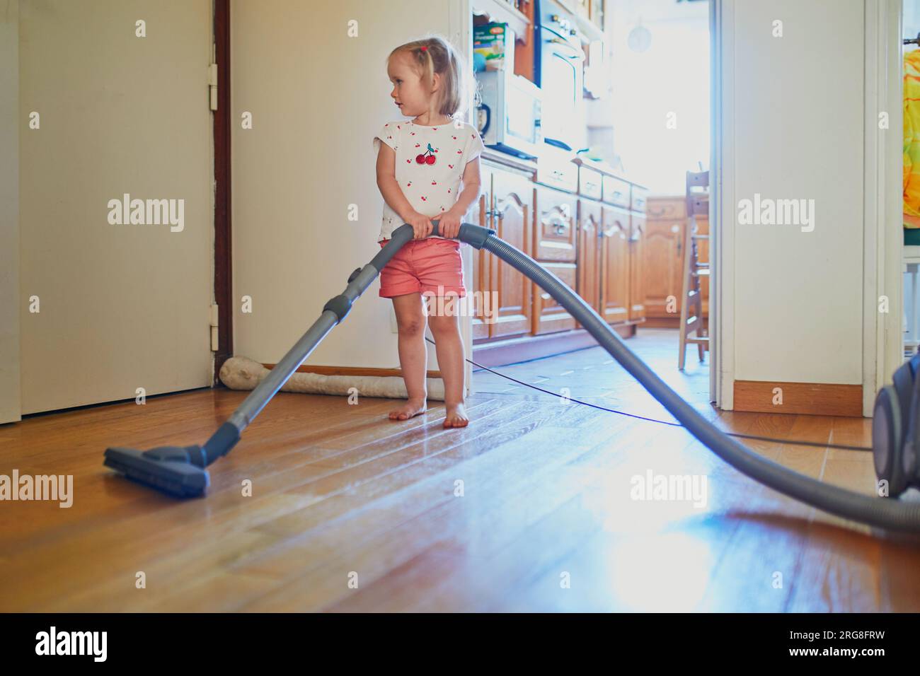 Adorable toddler girl using vacuum cleaner at home. Child helping
