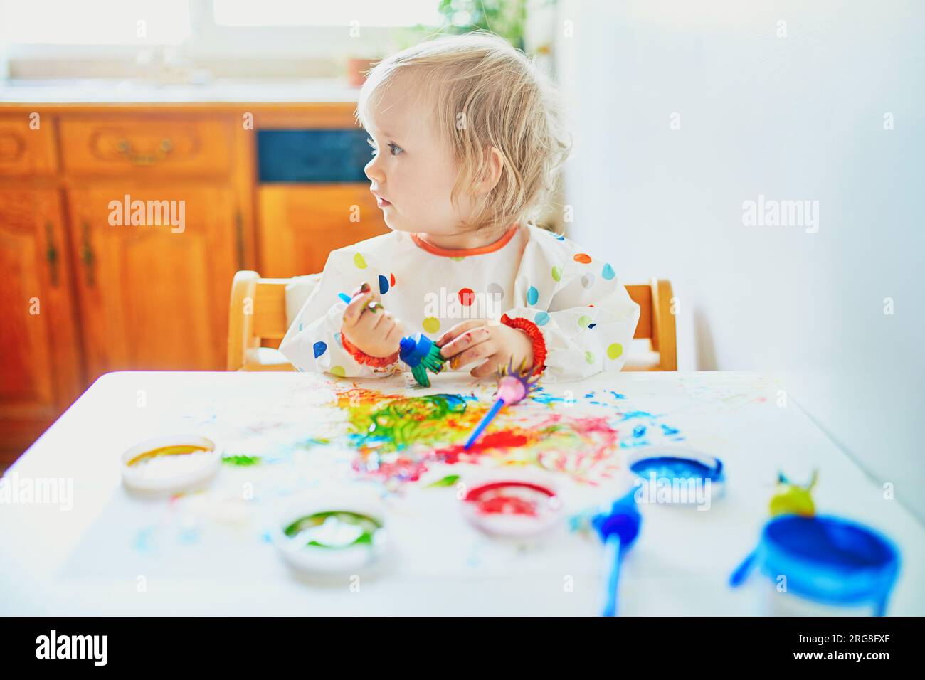 Adorable little girl painting with fingers at home, in kindergaten or preschool. Creative games for kids staying at home Stock Photo