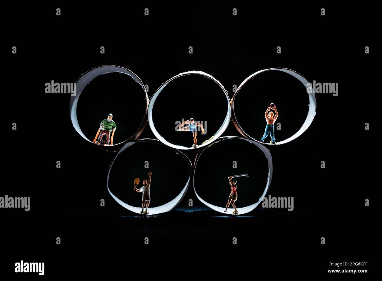 Olympics concept 5 Miniature sportsmen are standing in the Olympic rings symbol the sportswomen and sportsmen are posed as Running,  Athletics, Tennis Stock Photo