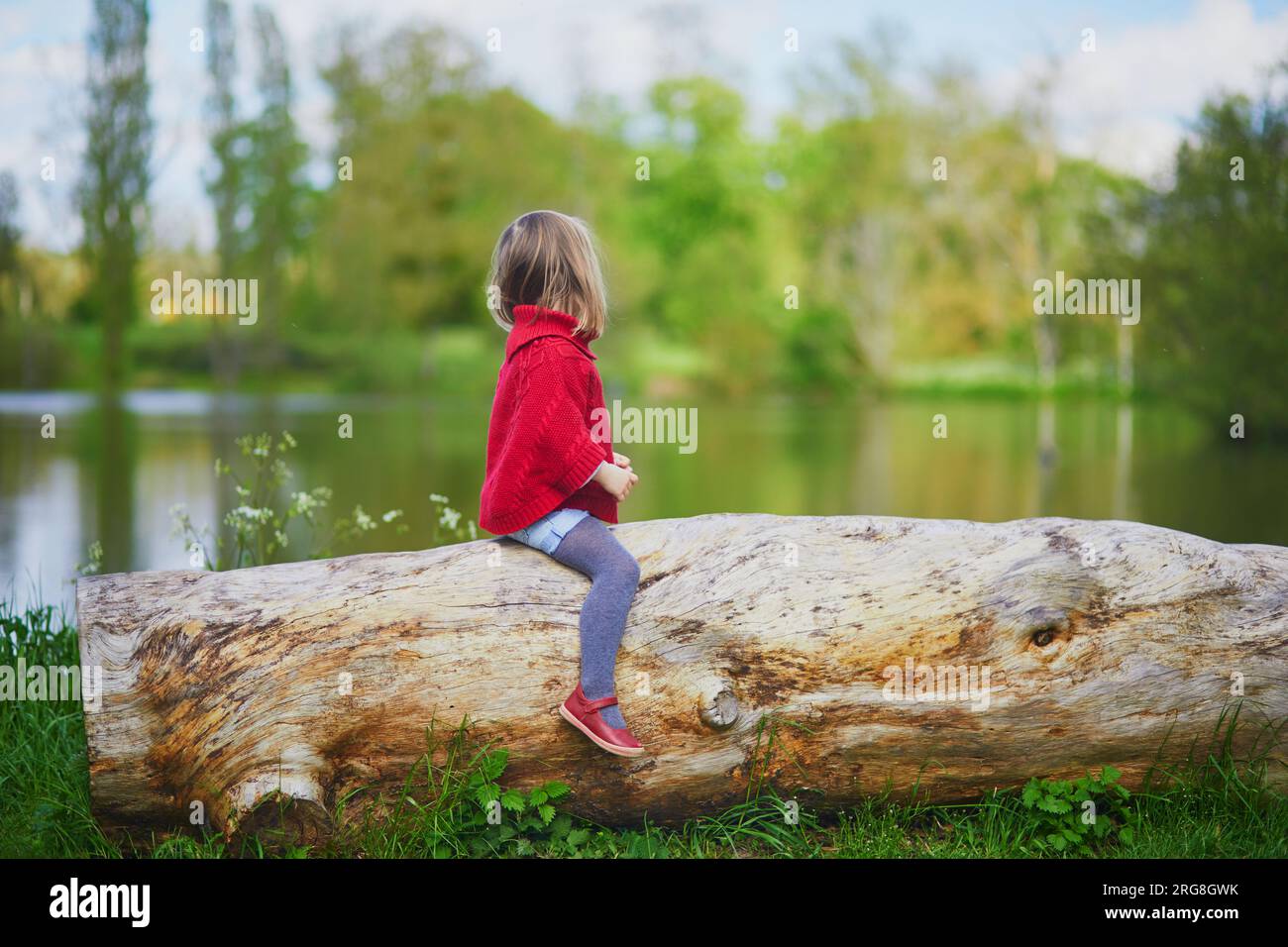 Adorable preschooler girl sitting on log and having fun in spring ...