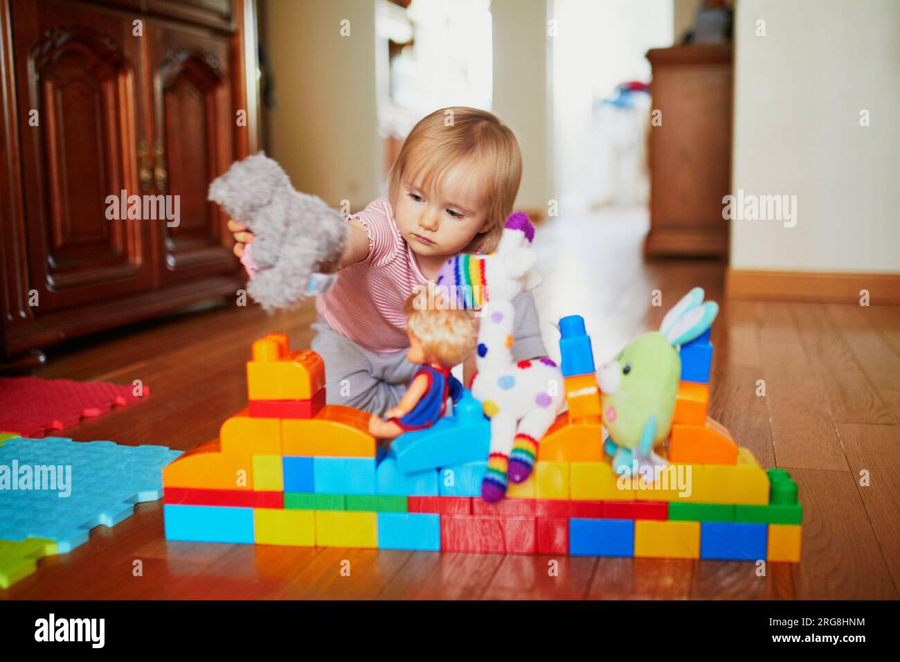 Adorable little girl playing with colorful plastic construction blocks