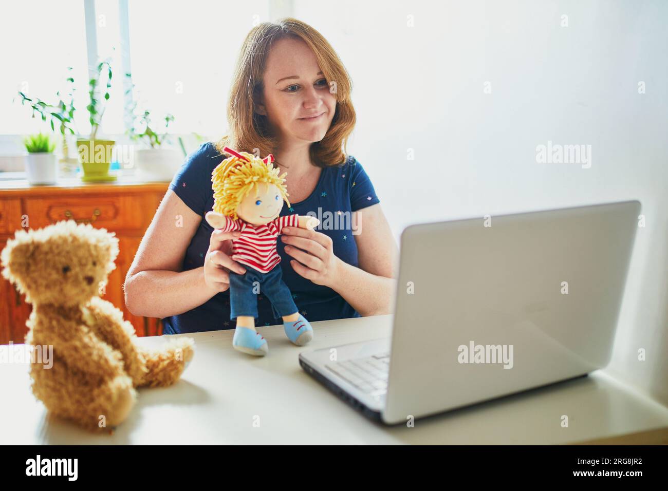 Kindergarten teacher in front of laptop having video conference chat with children. Woman entertaining little kids remotely. Online remote learning an Stock Photo