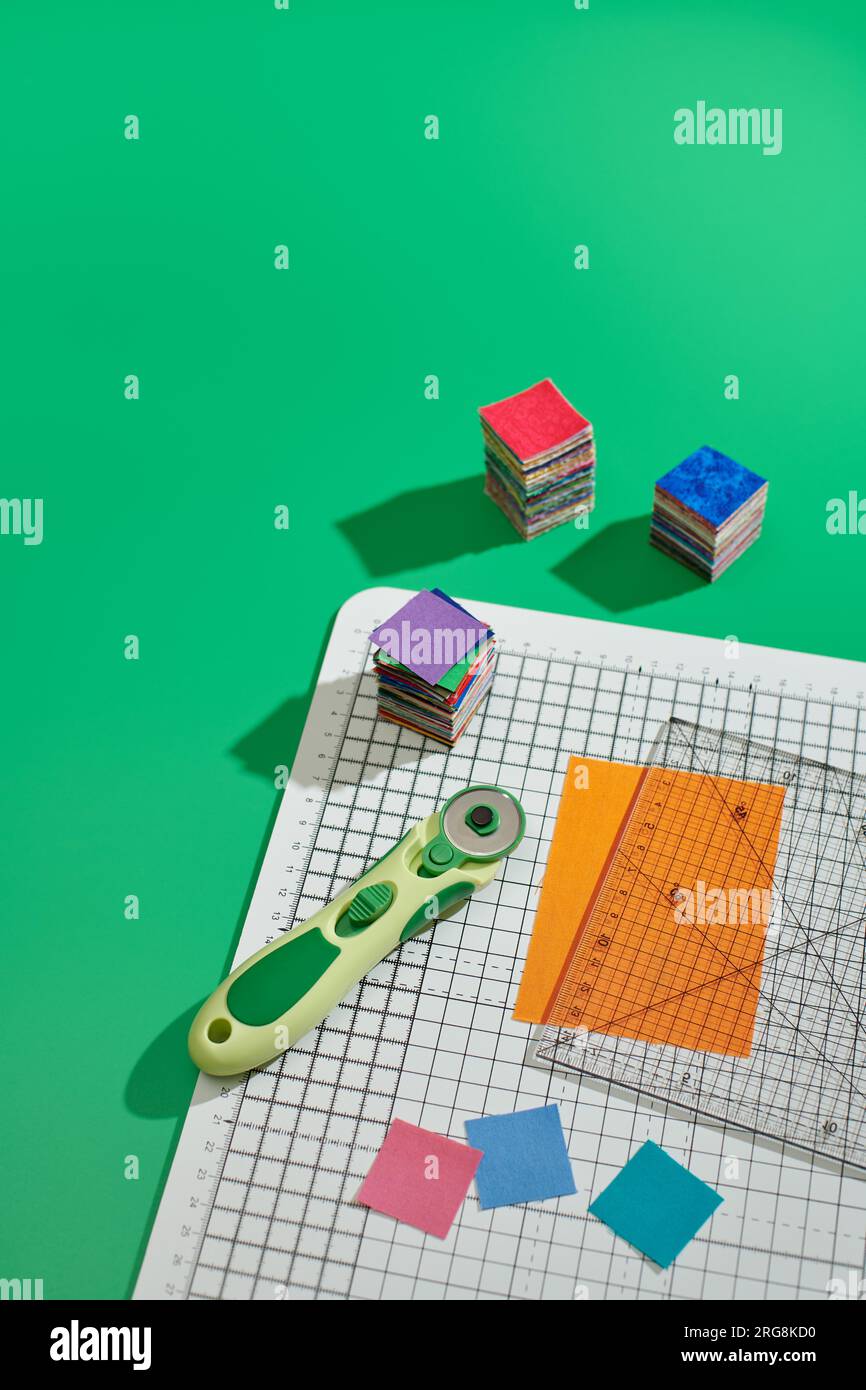 Rotary cutter, ruler, bright square pieces of fabric, stack of bright ...