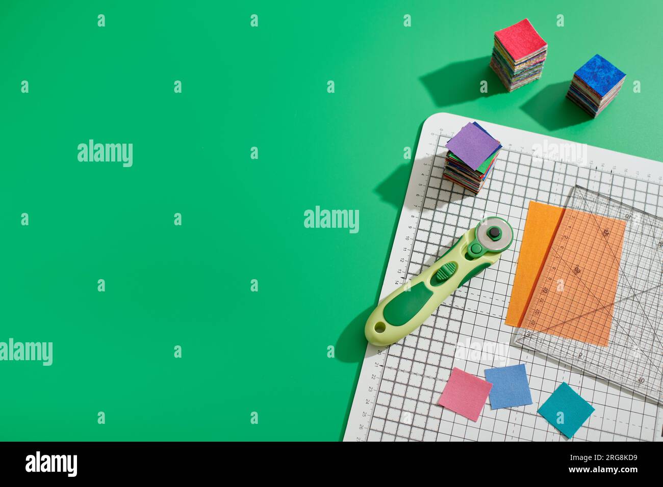 Rotary cutter, ruler, bright square pieces of fabric, stacks of bright ...