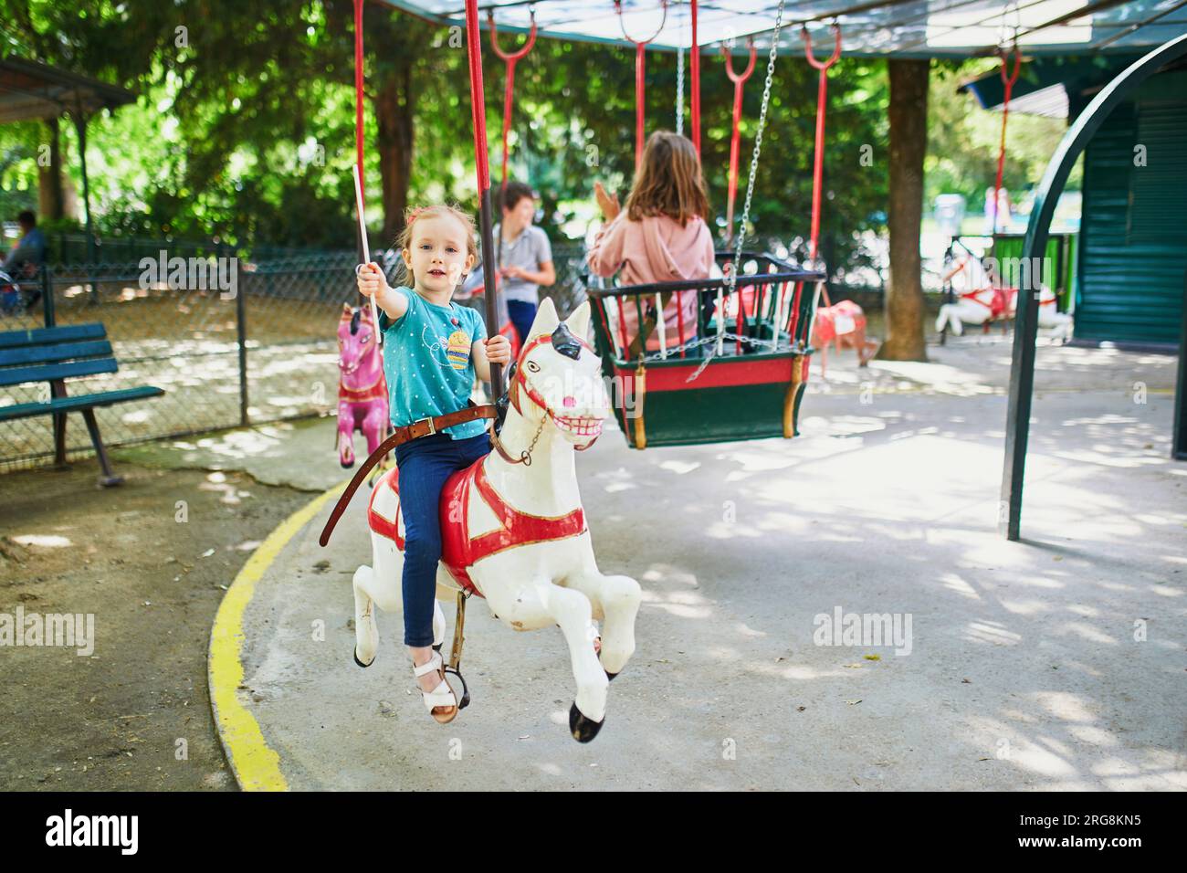 Adorable preschooler girl on a horse of traditional Parisian vintage merry-go-round where children have to catch and collect metallic rings with a sti Stock Photo
