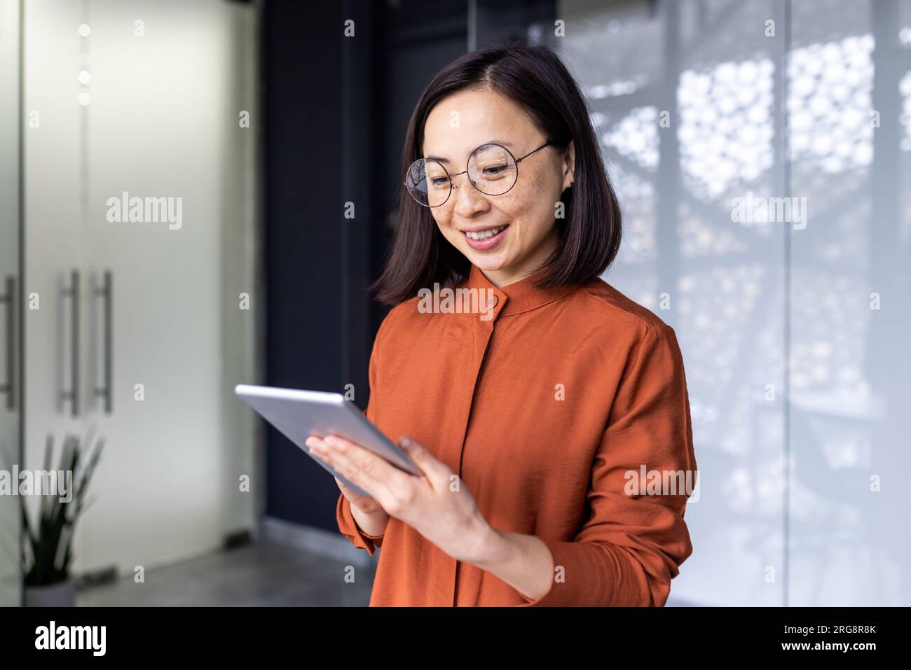 Smiling Asian young female programmer standing in office and working on tablet. Stock Photo