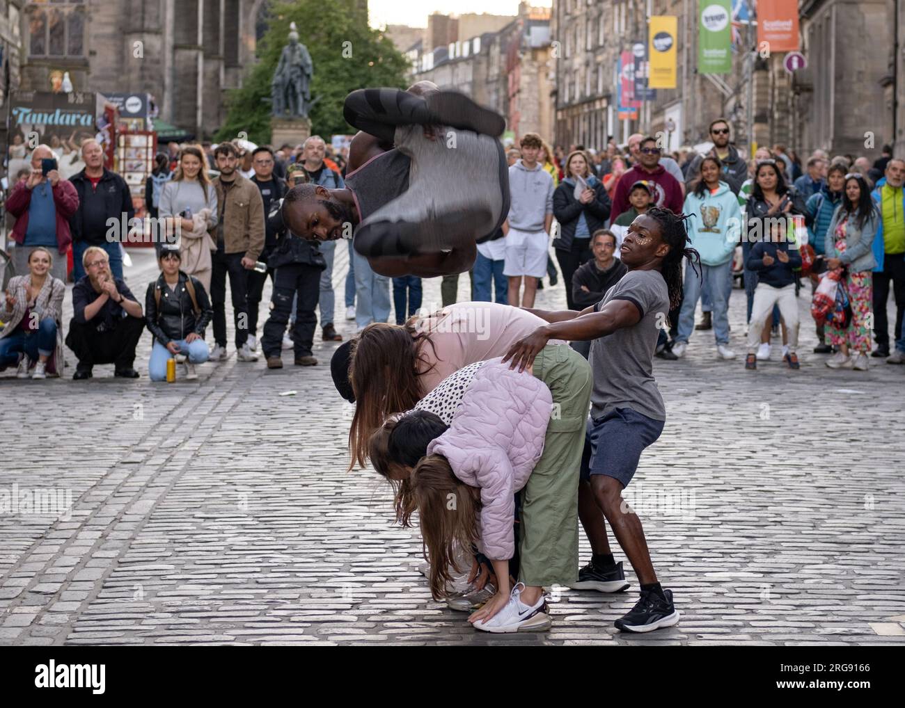 A member of Guinea act 'Afrique En Cirque' flies through air on the Royal Mile in Edinburgh during the Fringe Festival, August 2023. Scotland. Stock Photo