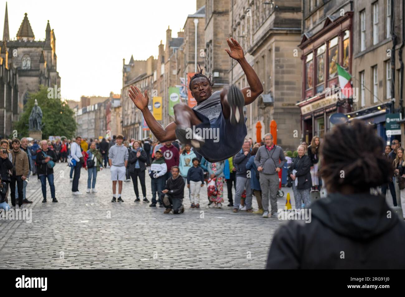 A member of Guinea act 'Afrique En Cirque' flies through air on the Royal Mile in Edinburgh during the Fringe Festival, August 2023. Scotland. Stock Photo
