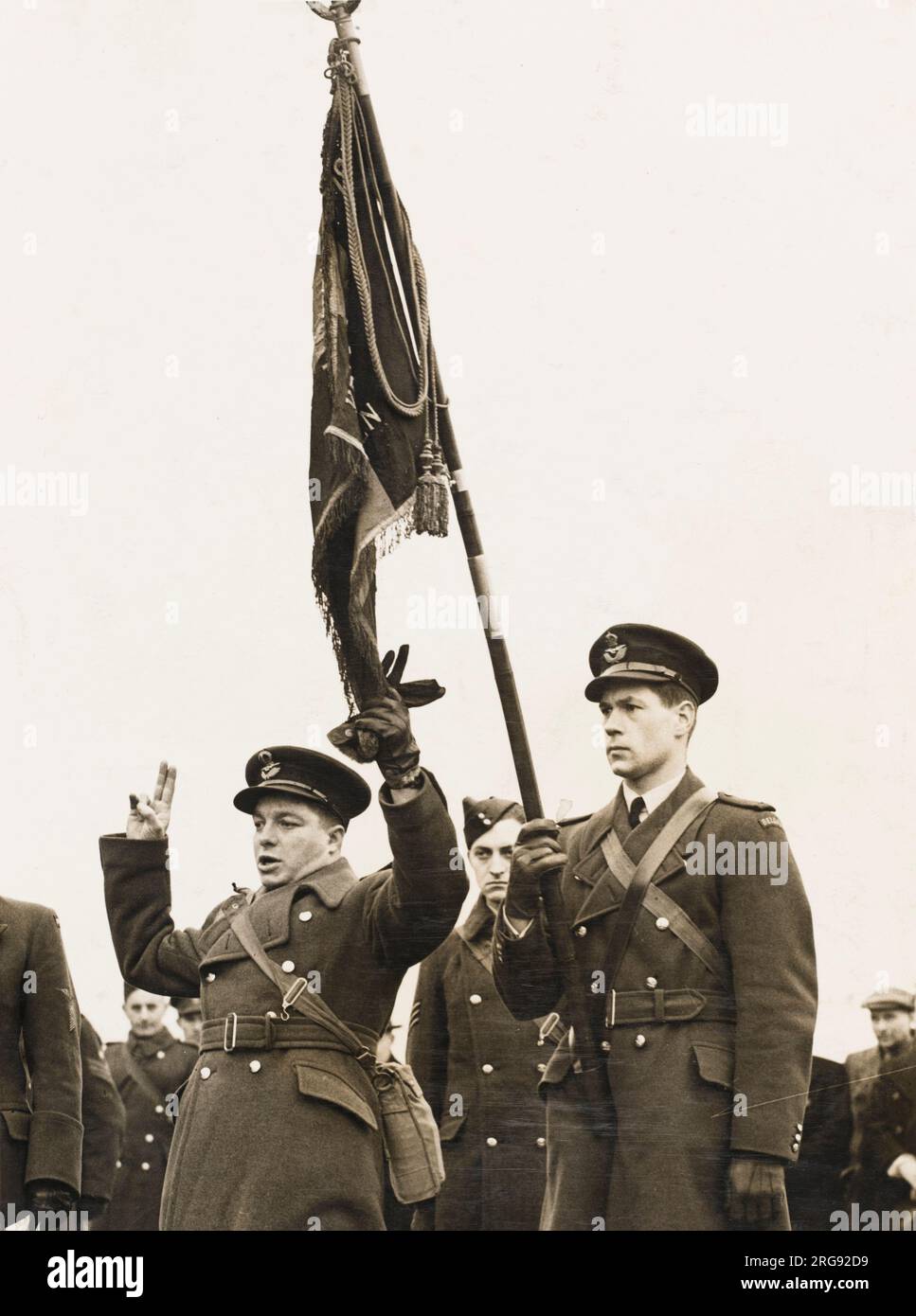 Two unnamed men risked their lives in a daring exploit to stand on the tarmac of an English aerodrome to salute the Belgian air force flag, a symbol of free men. The flag was given by the King of the Belgians to the Belgian Air Force, but when the Allied lines broke in 1940, German orders were to burn the flag. Disobeying orders, Air Force officers stuffed the flag into a shell case and buried it in the woods, where it was later retrieved by an observer in the Belgian Air Force. Stock Photo