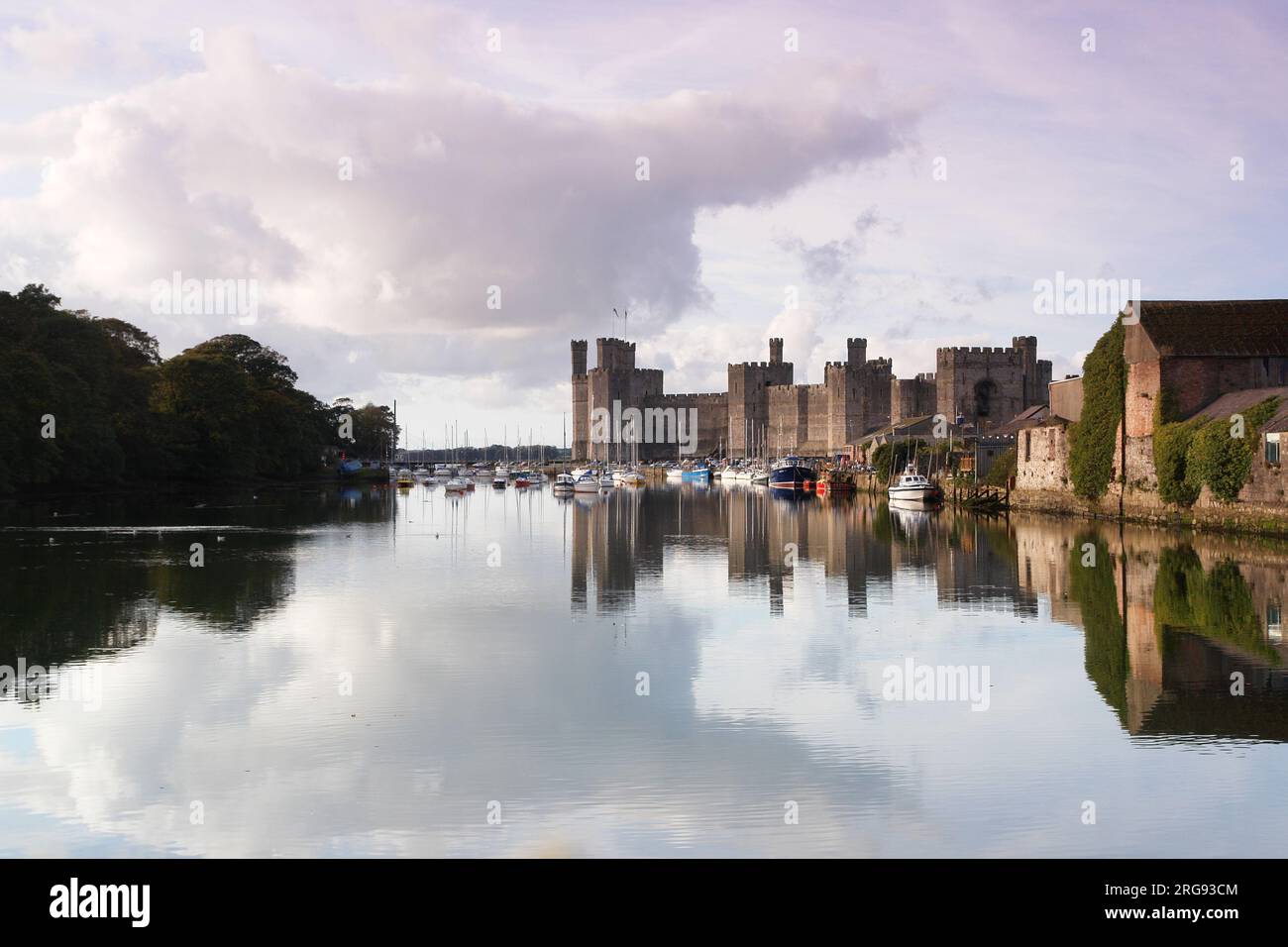 An atmospheric view of Caernarfon (Caernarvon) Castle in Gwynedd, North Wales, with numerous boats on the water.  The castle was built by the English King Edward I from around 1283, on the site of a Roman fortress and Norman motte. Stock Photo