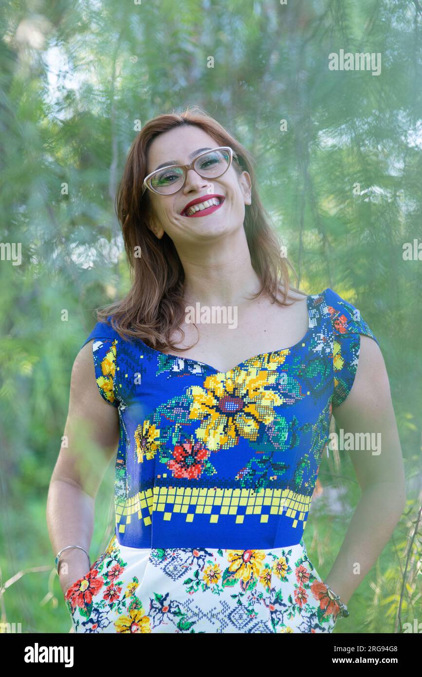 A pretty woman in a colorful dress and glasses smiles in green background Stock Photo