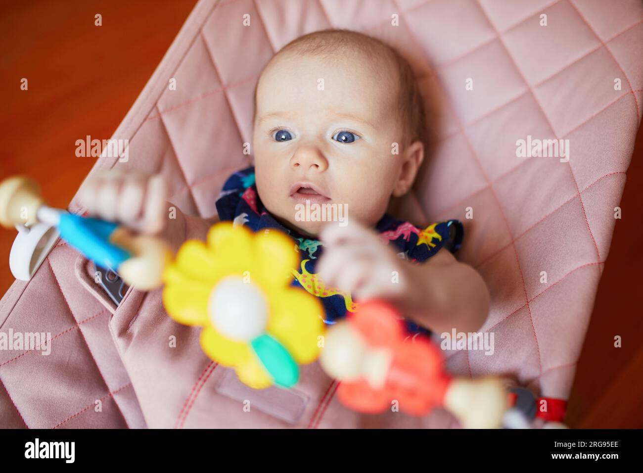 Adorable baby girl sitting in bouncer and playing with colorful toys Stock Photo