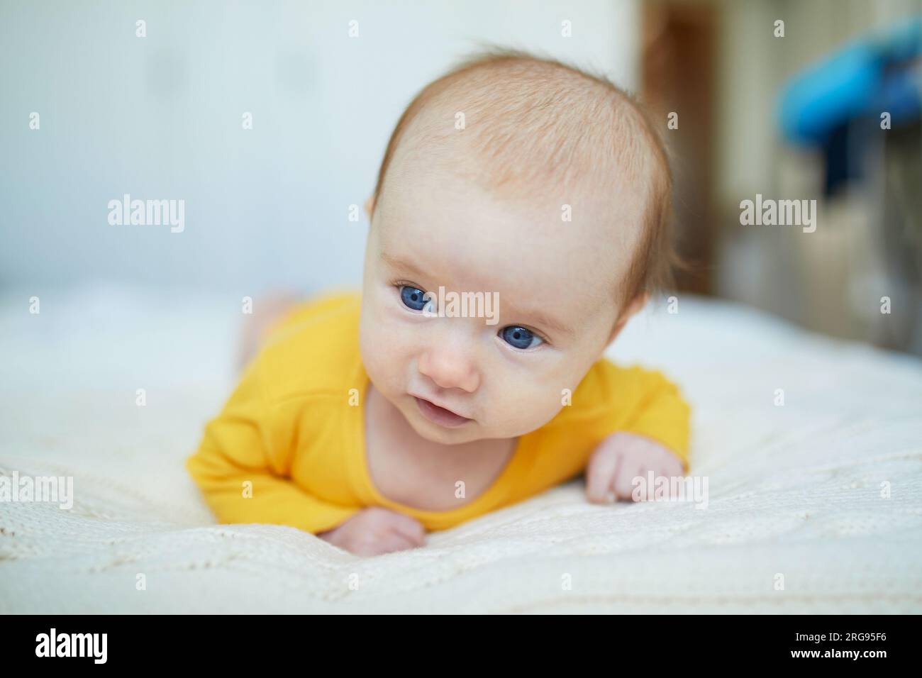 Adorable two months baby girl relaxing in bedroom on knitted blanket on a sunny morning. Newborn doing tummy time Stock Photo