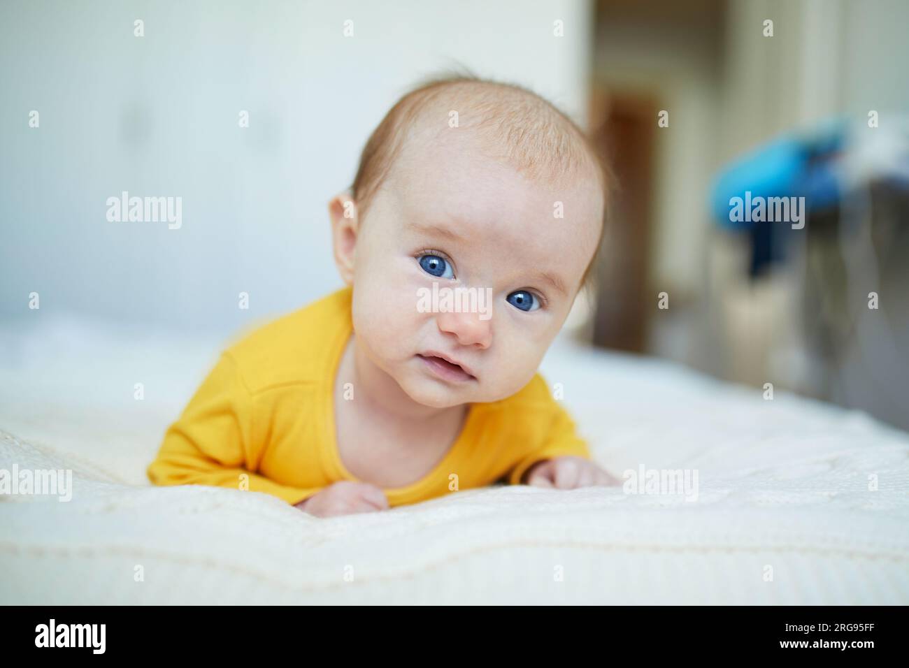 Adorable two months baby girl relaxing in bedroom on knitted blanket on a sunny morning. Newborn doing tummy time Stock Photo