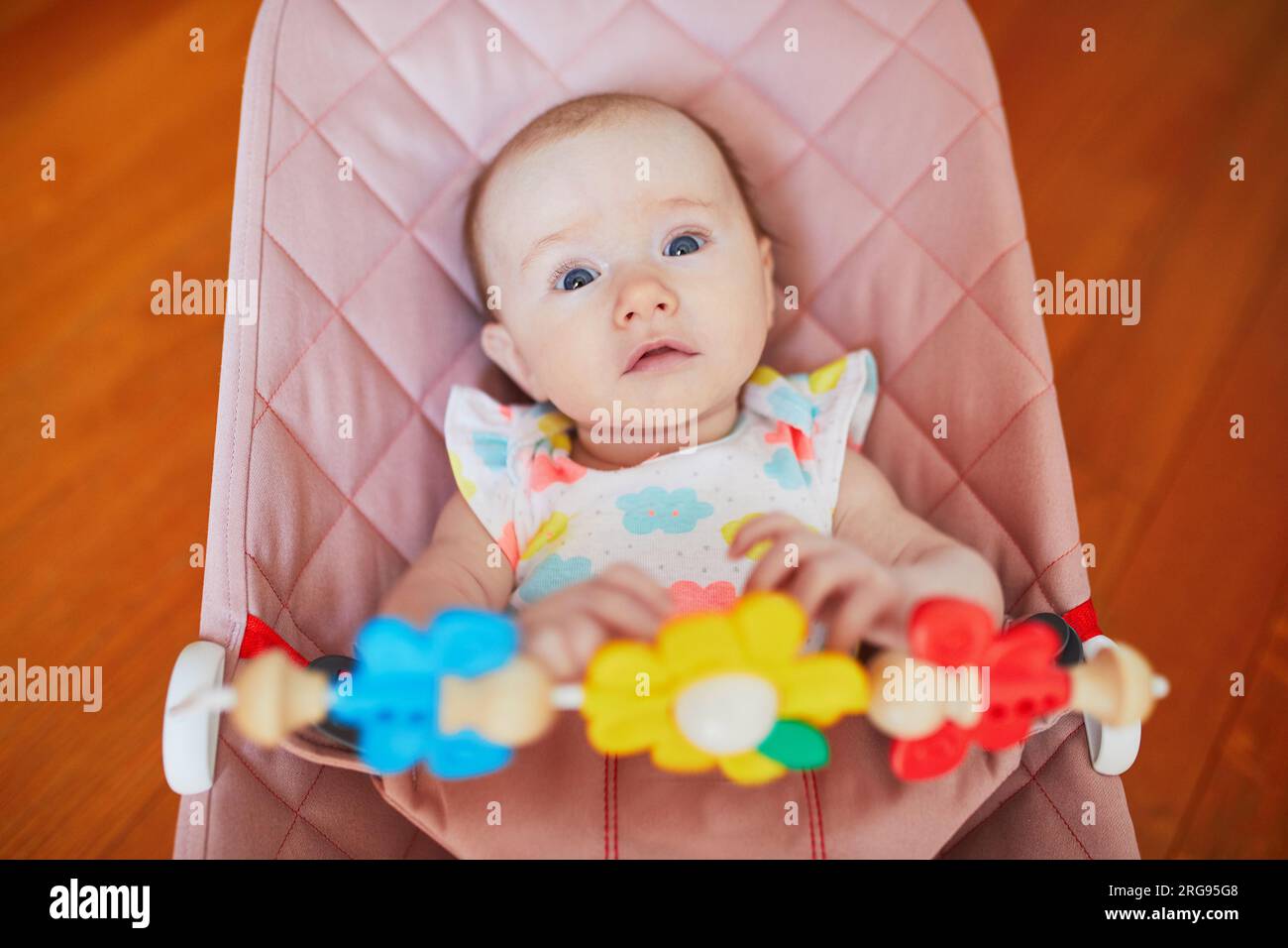Adorable baby girl sitting in bouncer and playing with colorful toys Stock Photo