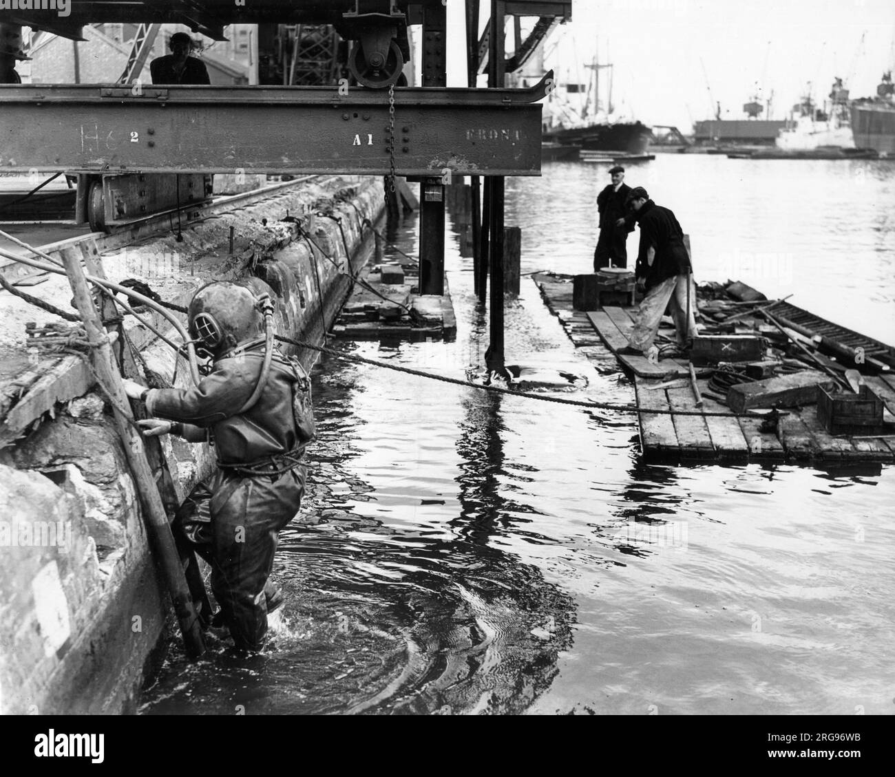 Dockside scene with two men on a raft, and a man in a heavy diving suit on the left, River Thames, Port of London. Stock Photo