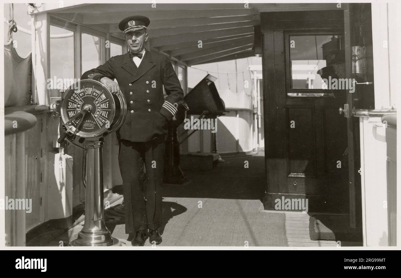 Royal Navy captain on the bridge of a warship, leaning on the brass engine room telegraph set at Full Ahead. Stock Photo