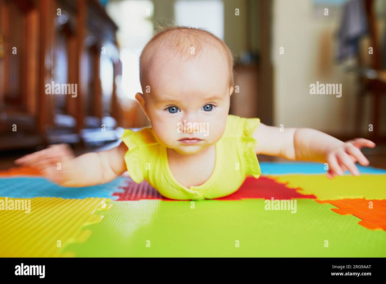 Adorable baby girl doing tummy time on colorful play mat Stock Photo