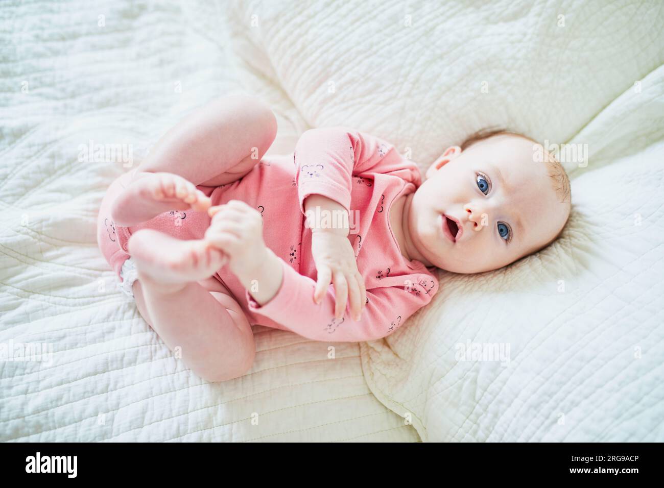 Adorable 4 months old baby girl lying on bed and touching her toes