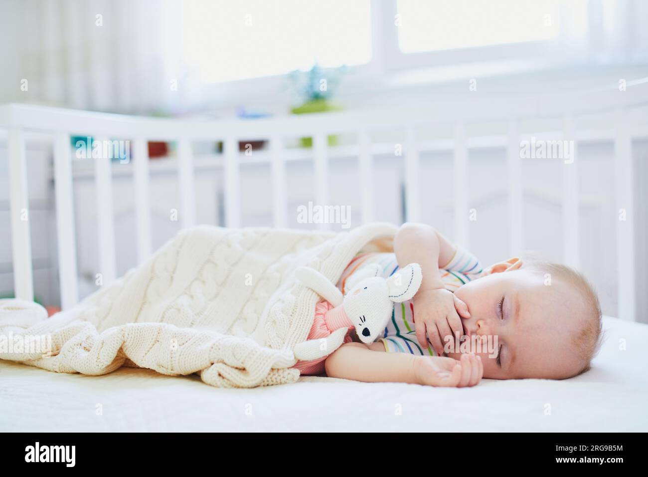 Adorable baby girl sleeping in cosleeper crib attached to parents' bed