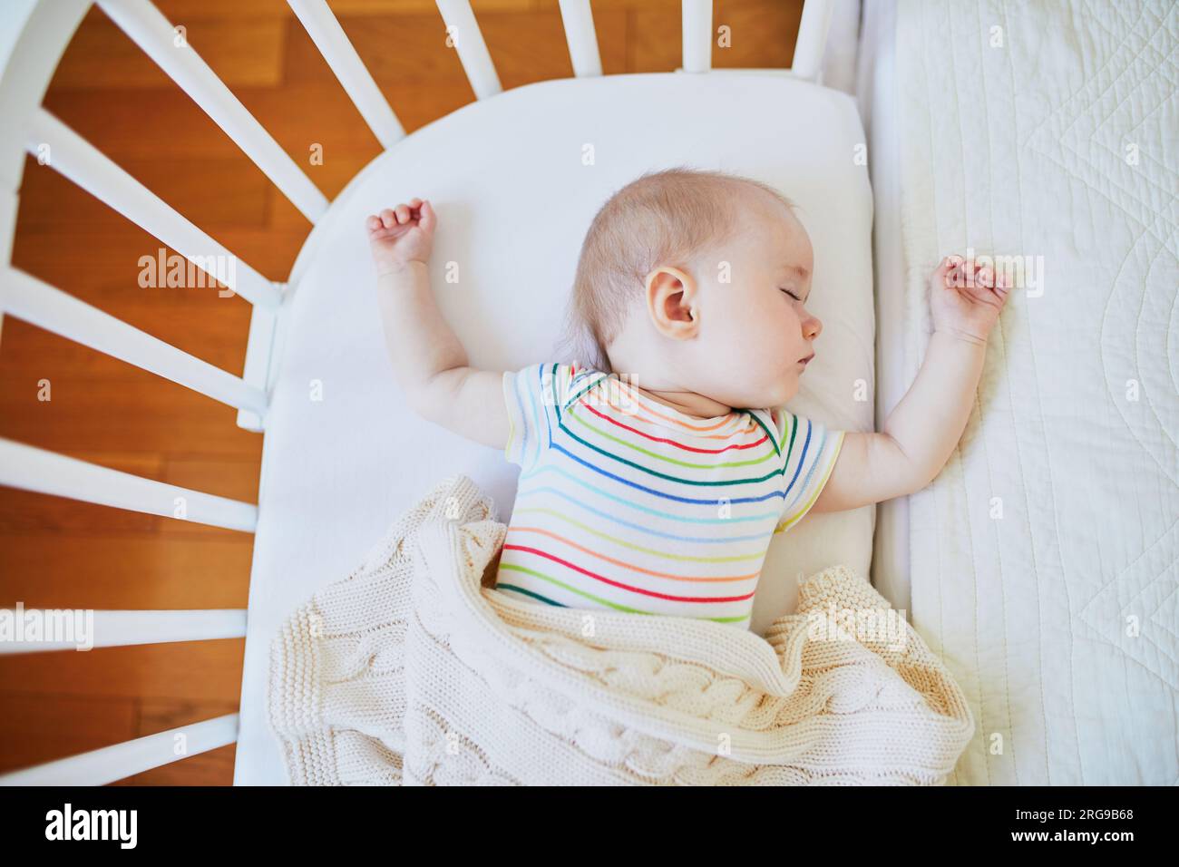 Adorable baby girl sleeping in cosleeper crib attached to parents' bed