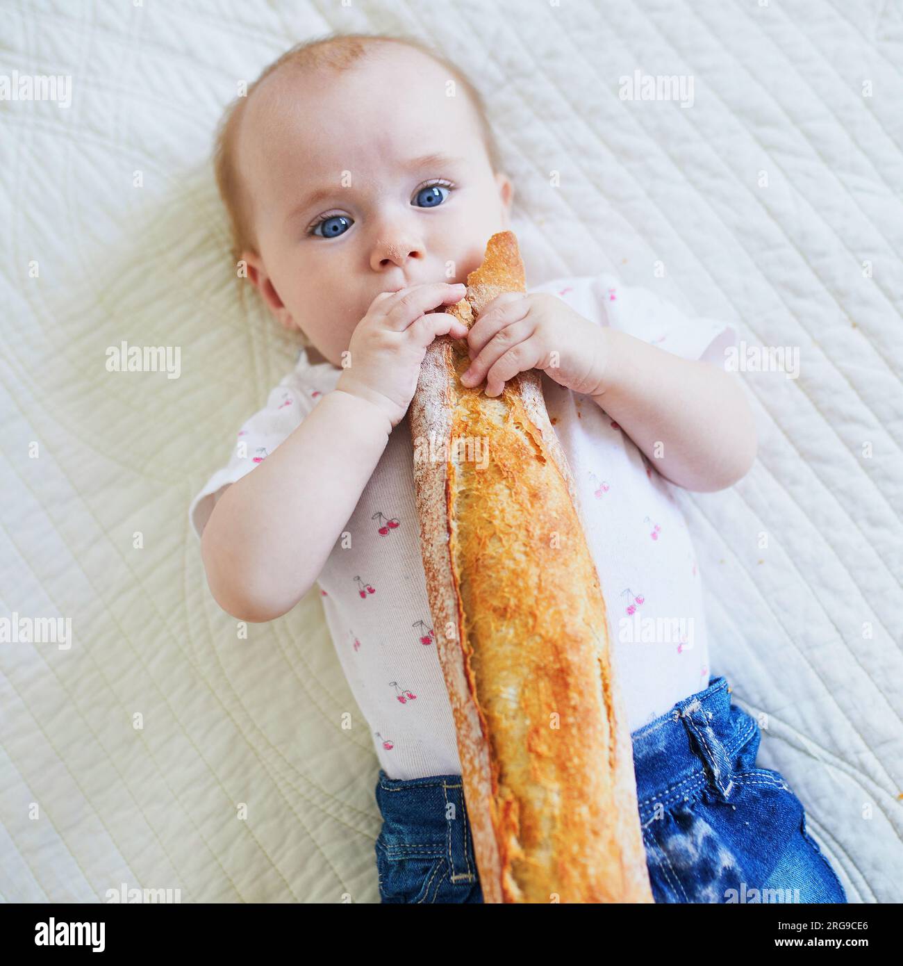 Six months old baby girl eating traditional French bread (baguette