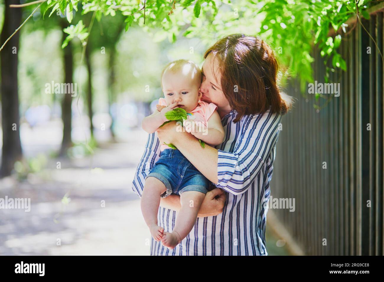 Happy young woman holding her little baby girl outdoors. Mother walking with daughter on a summer day Stock Photo