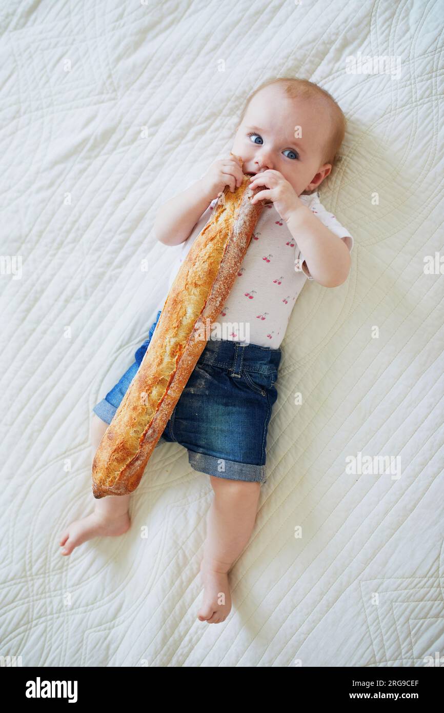 Six months old baby girl eating traditional French bread (baguette
