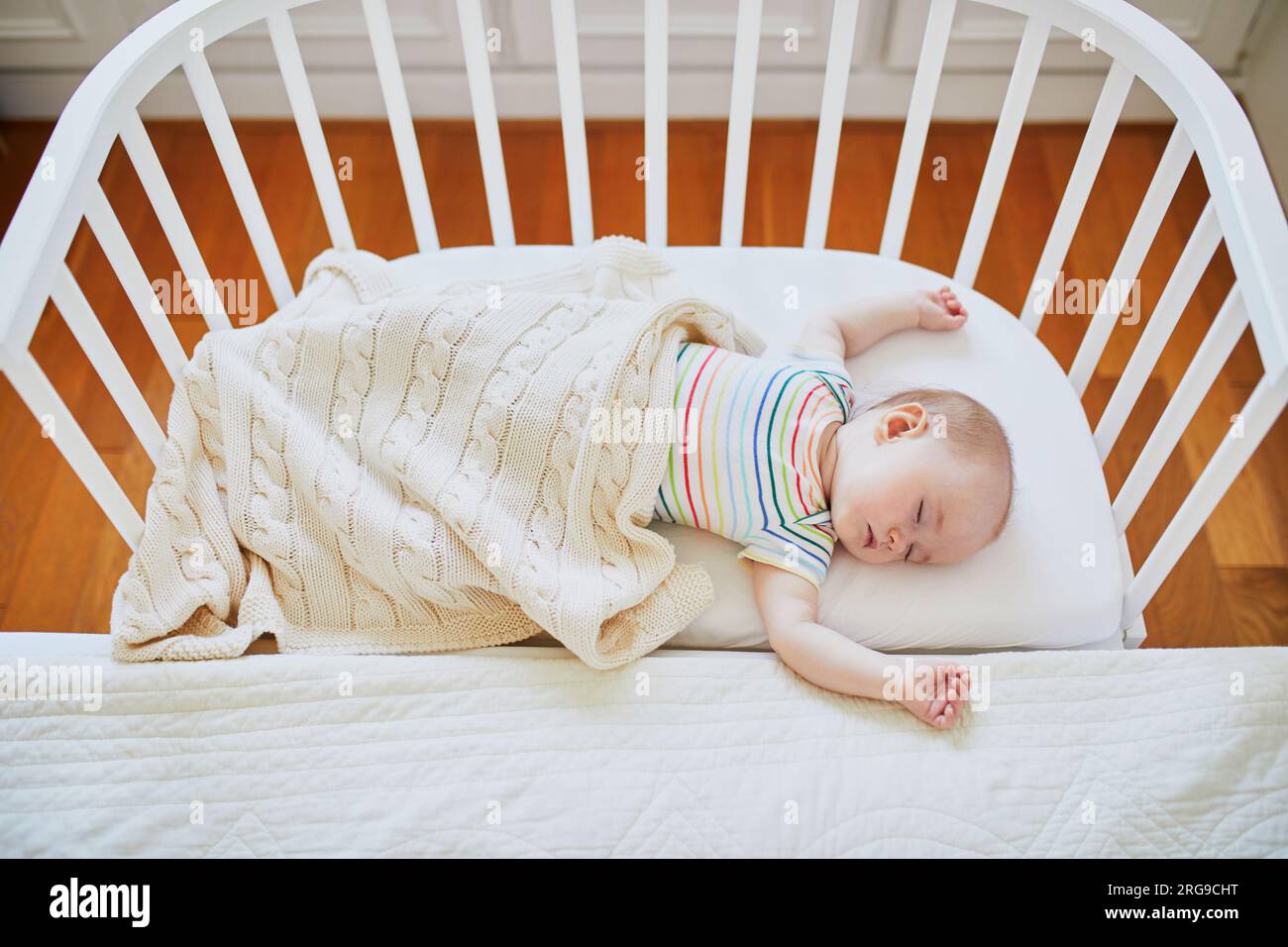 Adorable baby girl sleeping in cosleeper crib attached to parents' bed