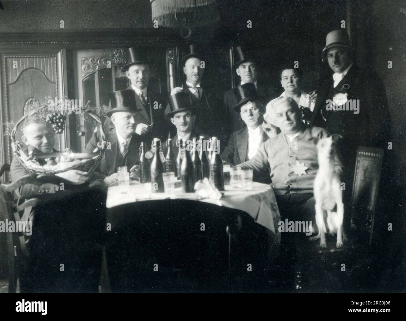 A jolly men's drinking club - the table is well stocked with beer and glasses and everyone is very smartly-dressed in top hats ans suits, some with additonal 'badges of office'! Stock Photo