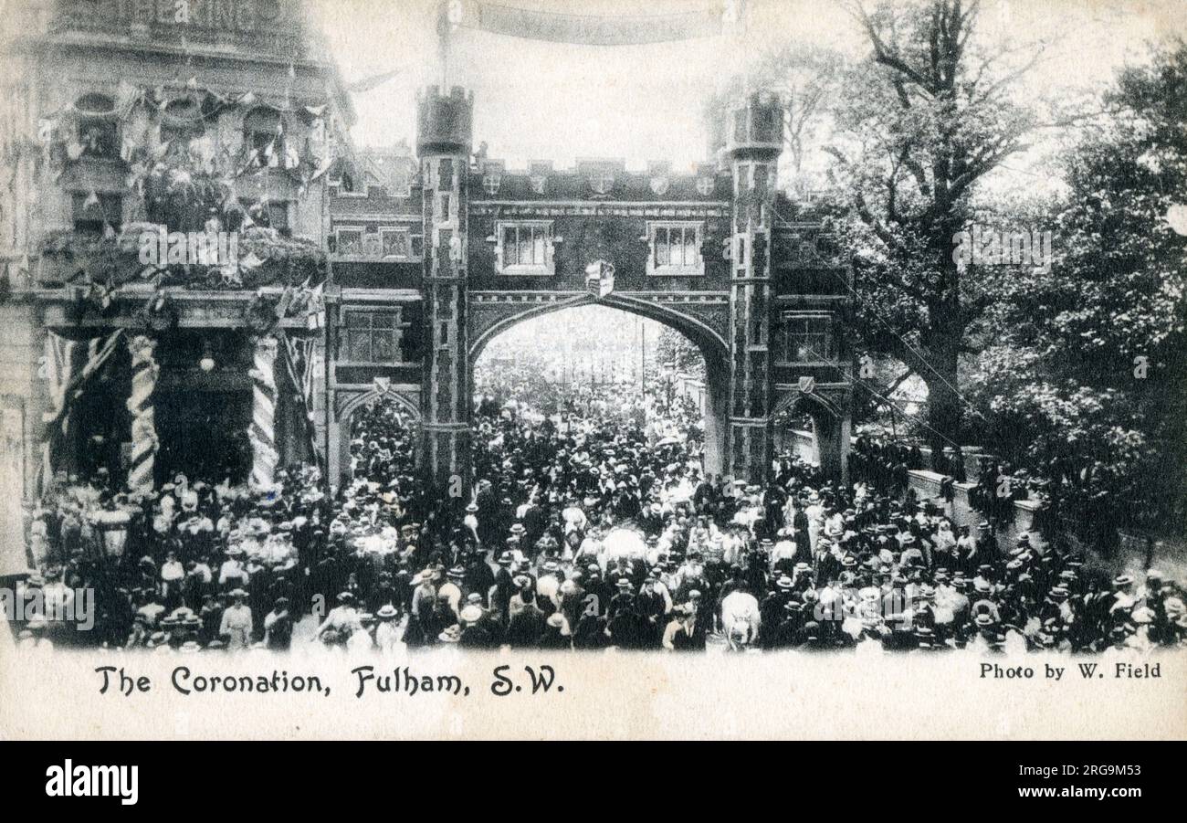 Celebrating the coronation of King Edward VII in Fulham, West London - decorations adorning the streetside buildings and crowds gathering beneath and around a temporary arch across the street. Stock Photo