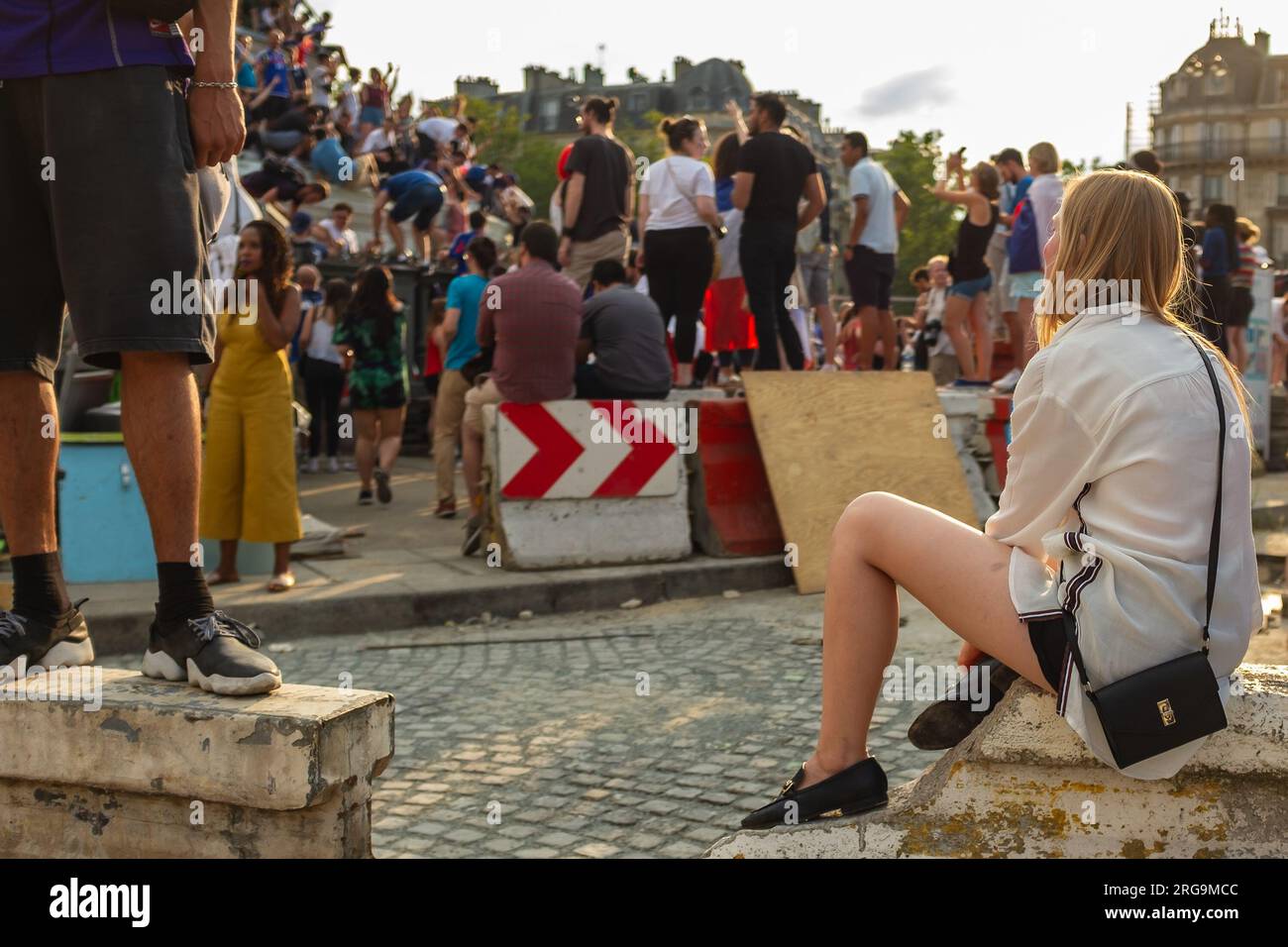 Paris, France, 2018. A blonde preppy girl is sitting amidst the chaos place de la Bastille, the day France won the soccer World Cup Stock Photo