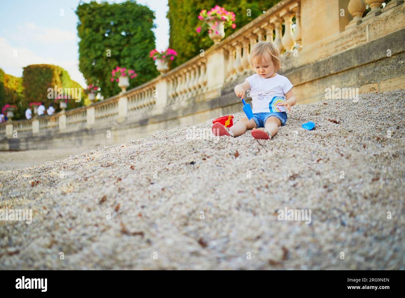 Little girl sitting on a large heap of stones and playing with pebbles ...