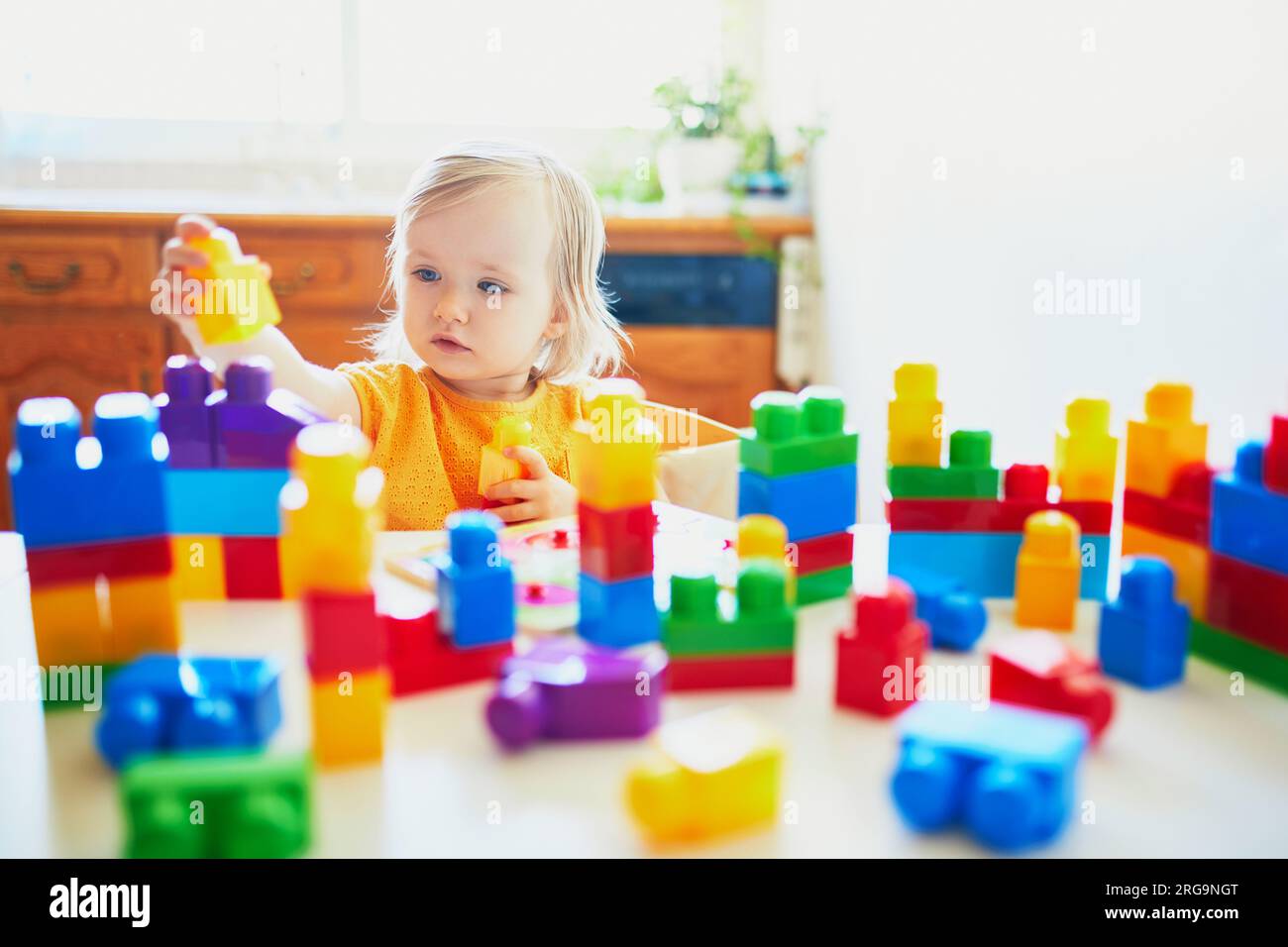 Adorable little girl playing with colorful plastic construction blocks ...