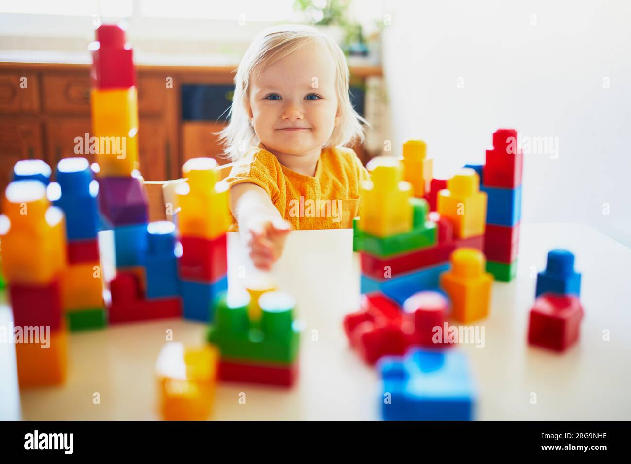 Adorable little girl playing with colorful plastic construction blocks ...