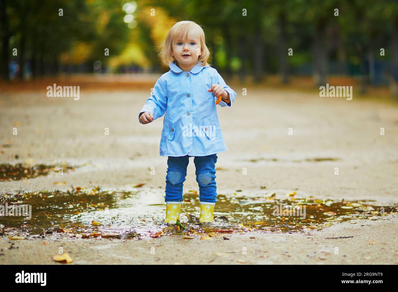 Child wearing yellow rain boots and jumping in puddle on a fall day ...