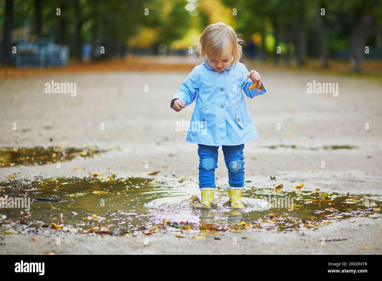 Child wearing yellow rain boots and jumping in puddle on a fall day ...