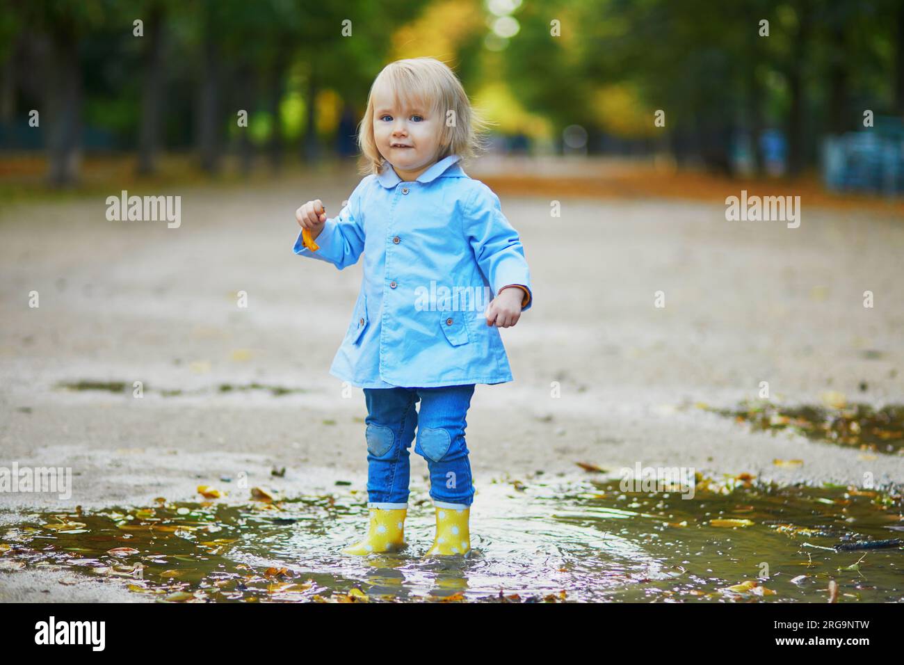 Child wearing yellow rain boots and jumping in puddle on a fall day ...