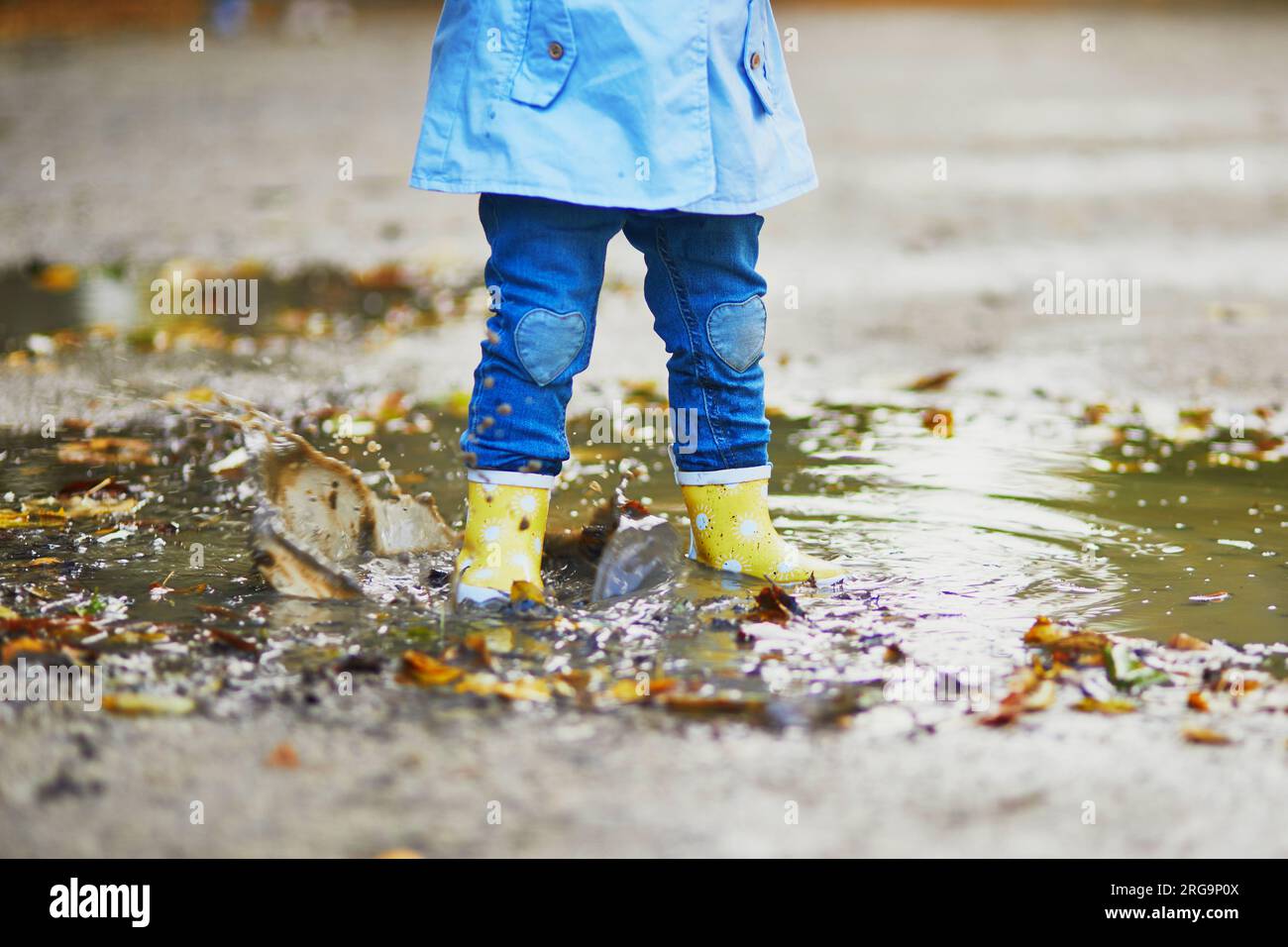 Child wearing yellow rain boots and jumping in puddle on a fall day ...